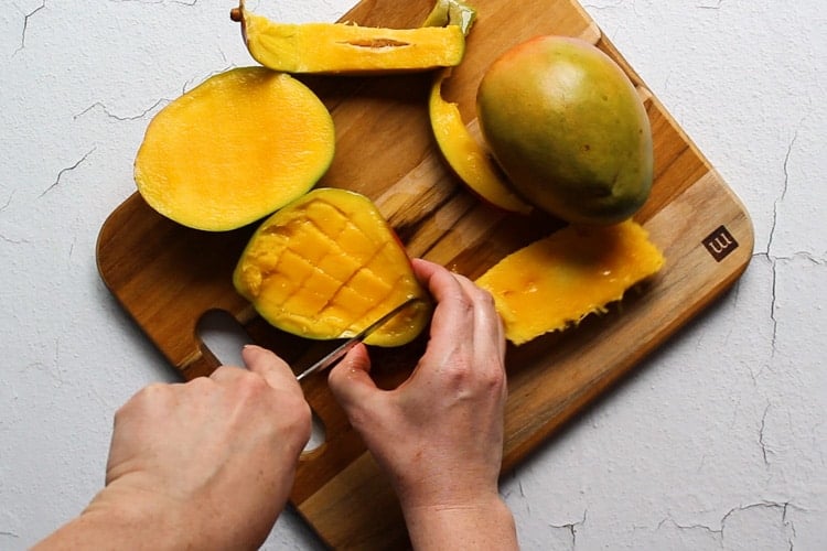 Hands slicing mango with a knife on a cutting board