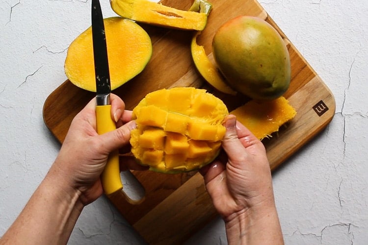 Hands fanning out sliced mango on a cutting board