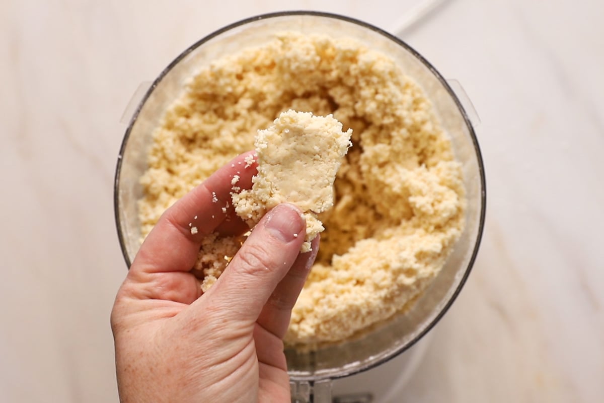 Pie crust dough held in a hand over a food processor