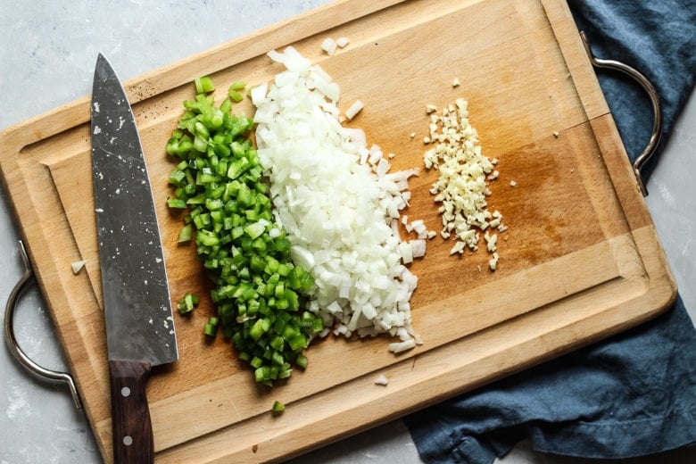 Instant pot chili recipe ingredients, green bell peppers, onion, and garlic chopped on a cutting board