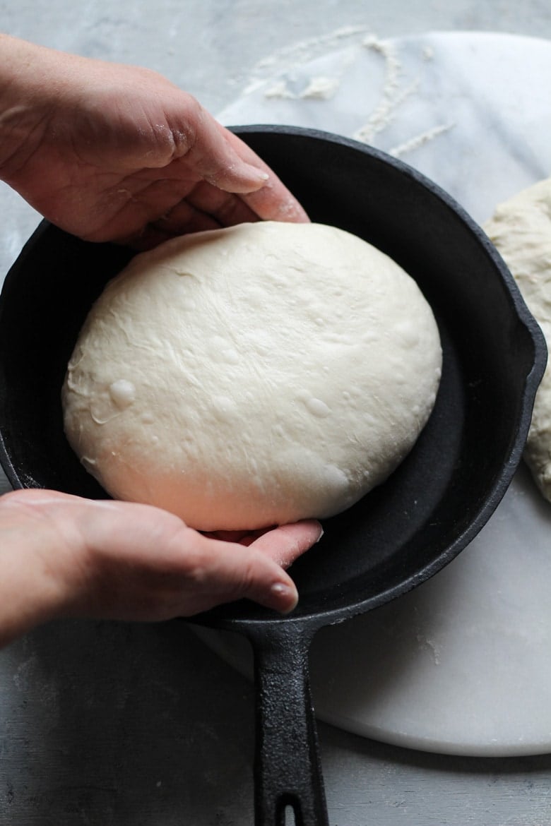 Round or boule sourdough bread dough placed in a cast iron skillet for baking