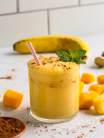 Mango Lassi Smoothie in a glass with mango slices and a banana