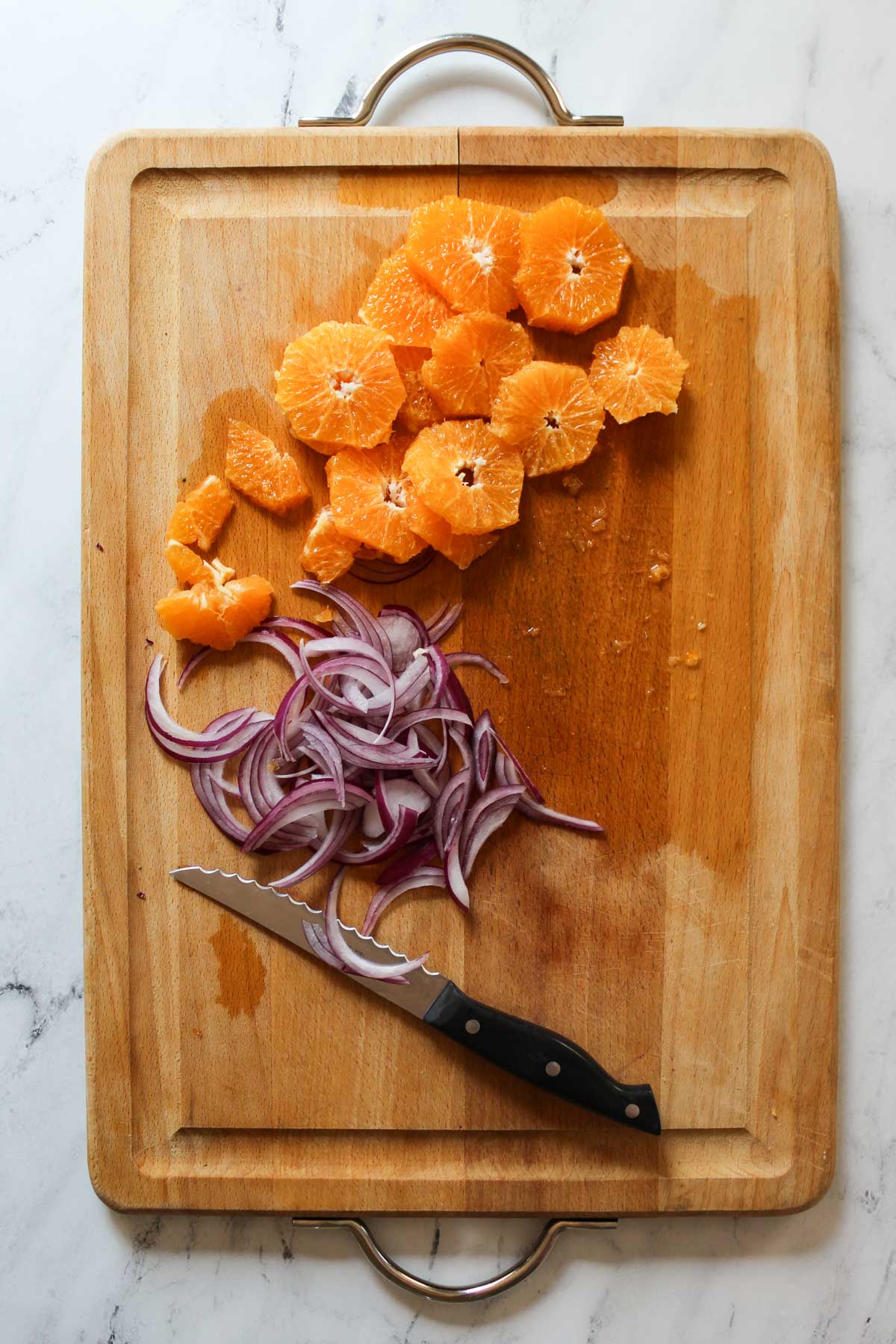 Sliced oranges and red onions on a cutting board with a knife