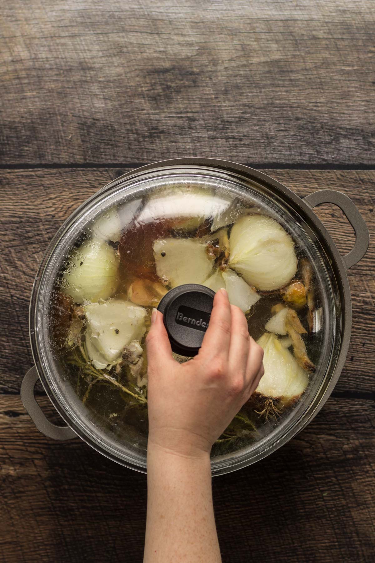 A hand covering a lid of a stock pot