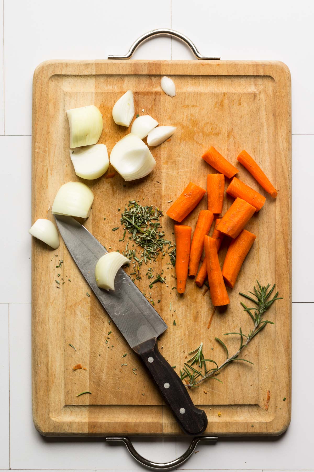 Chopped carrots, onions, and rosemary on a cutting board