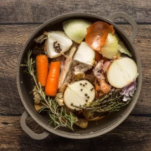 Chicken stock in a pot with onions, carrots, and herbs