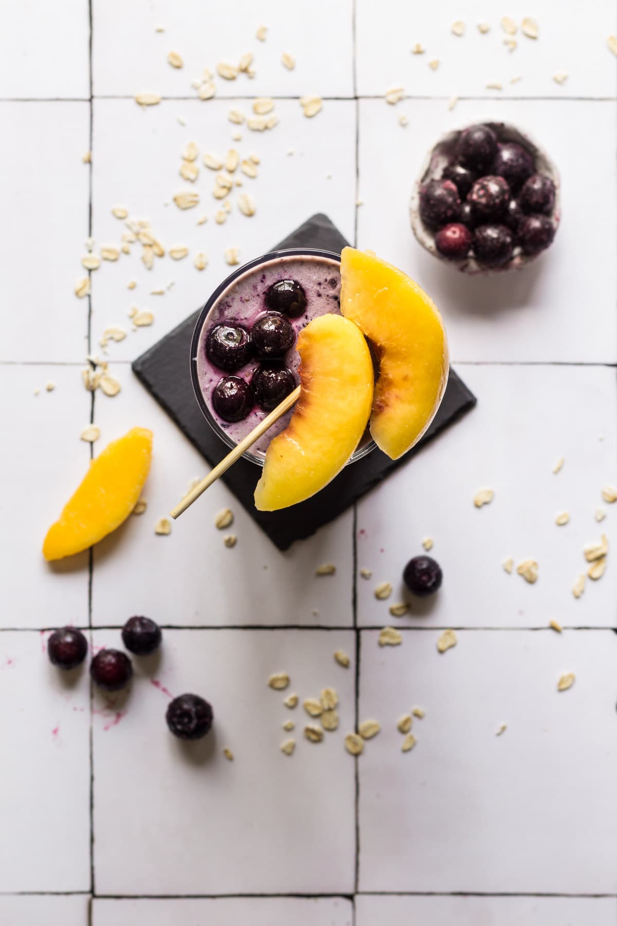 Blueberry smoothie in a glass topped with peaches and a bowl of blueberries