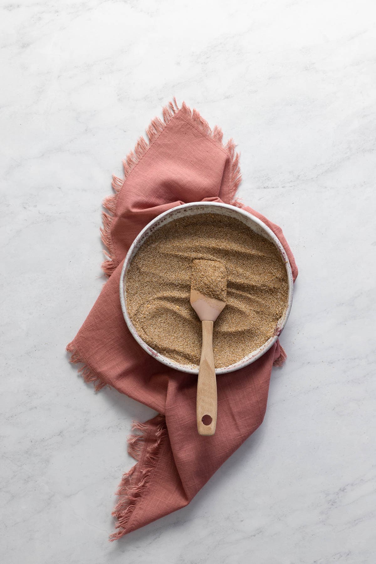 A bowl of chai spices with a spatula and pink napkin