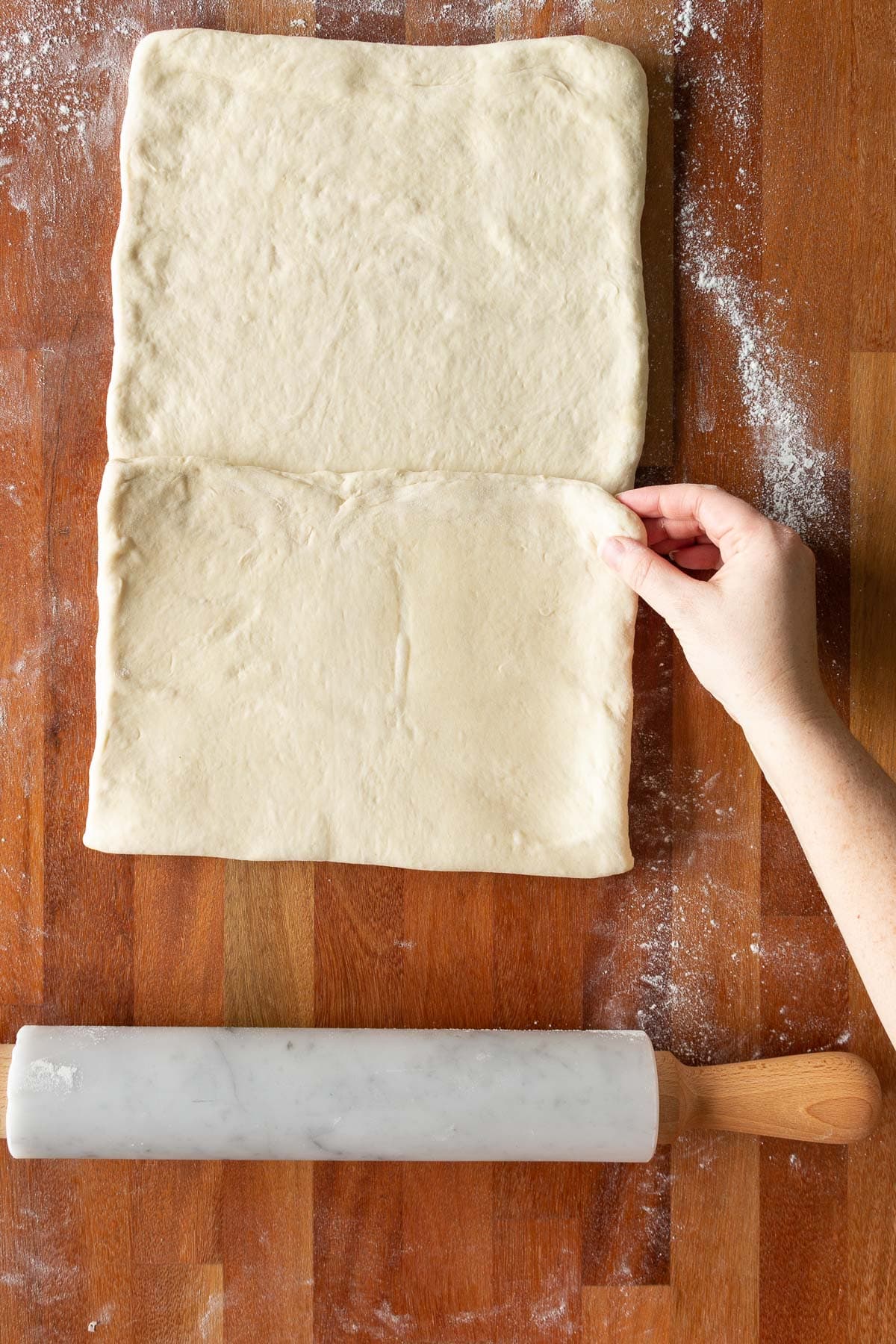 A hand folding croissant dough into thirds