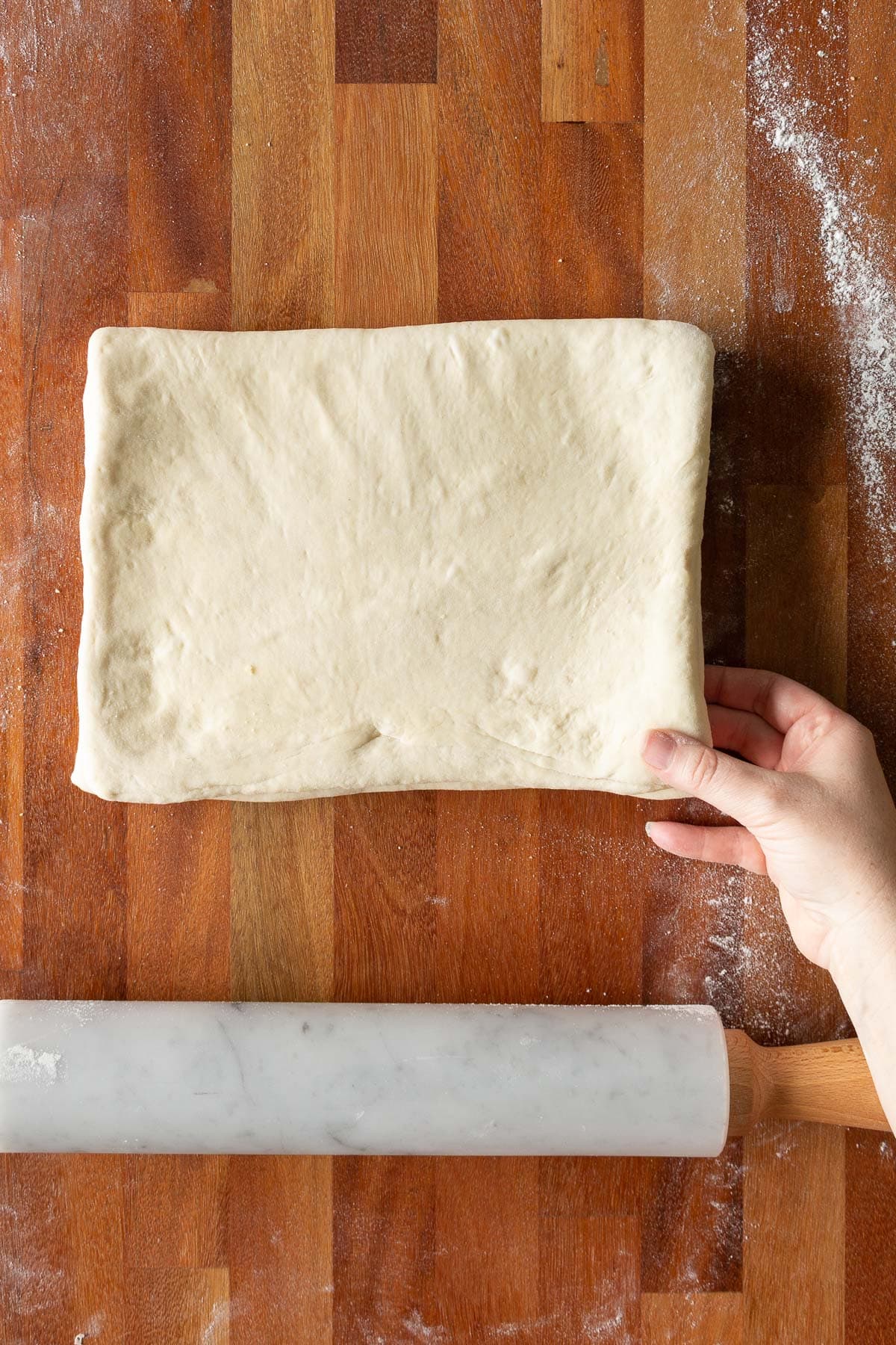 A hand folding croissant dough like a book