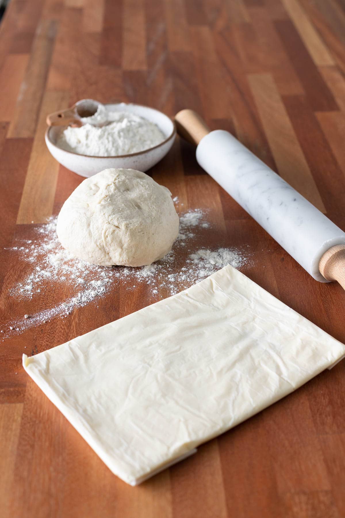 Ball of croissant dough and butter rectangle with a rolling pin and flour