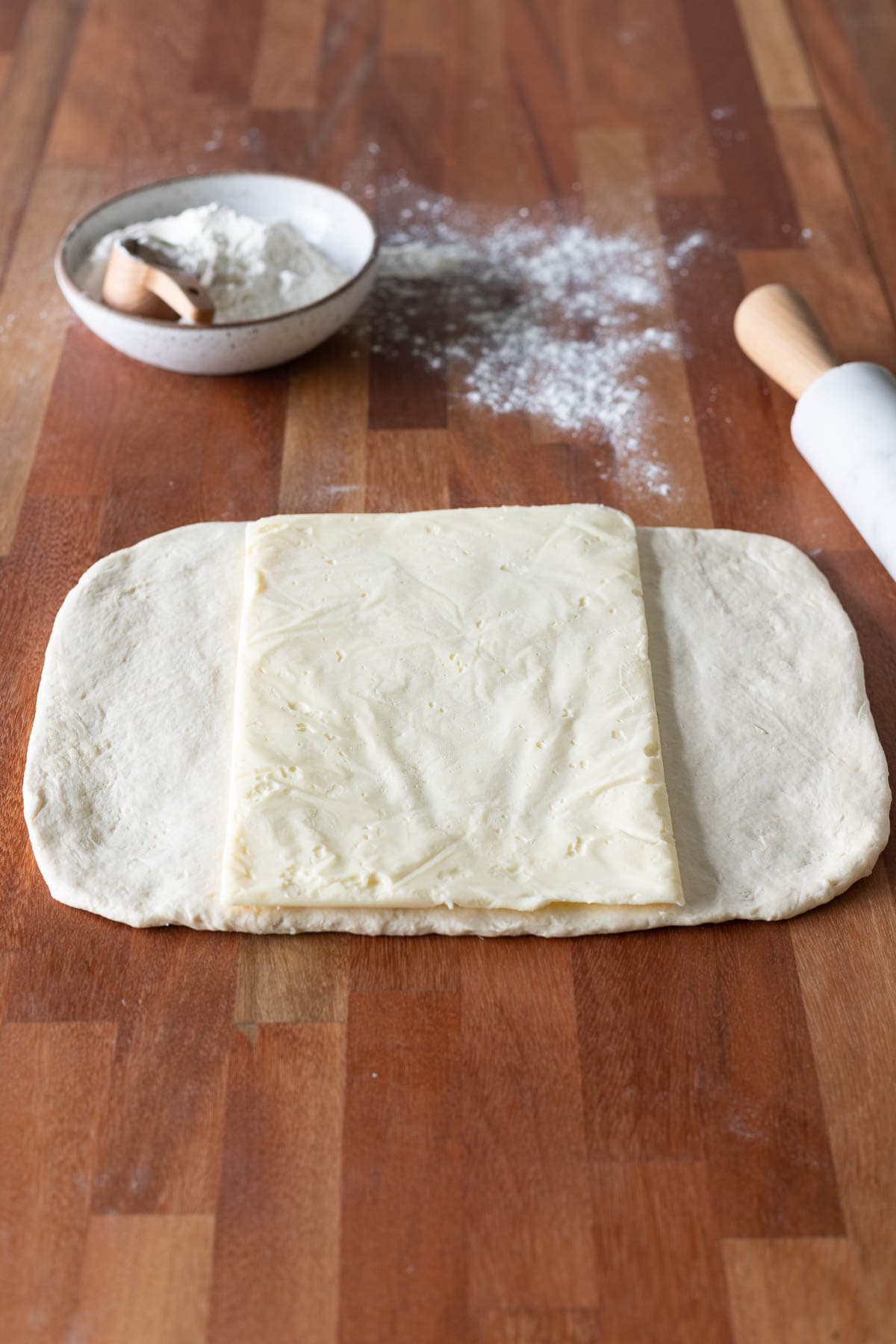 Butter rectangle inside croissant dough with a bowl of flour