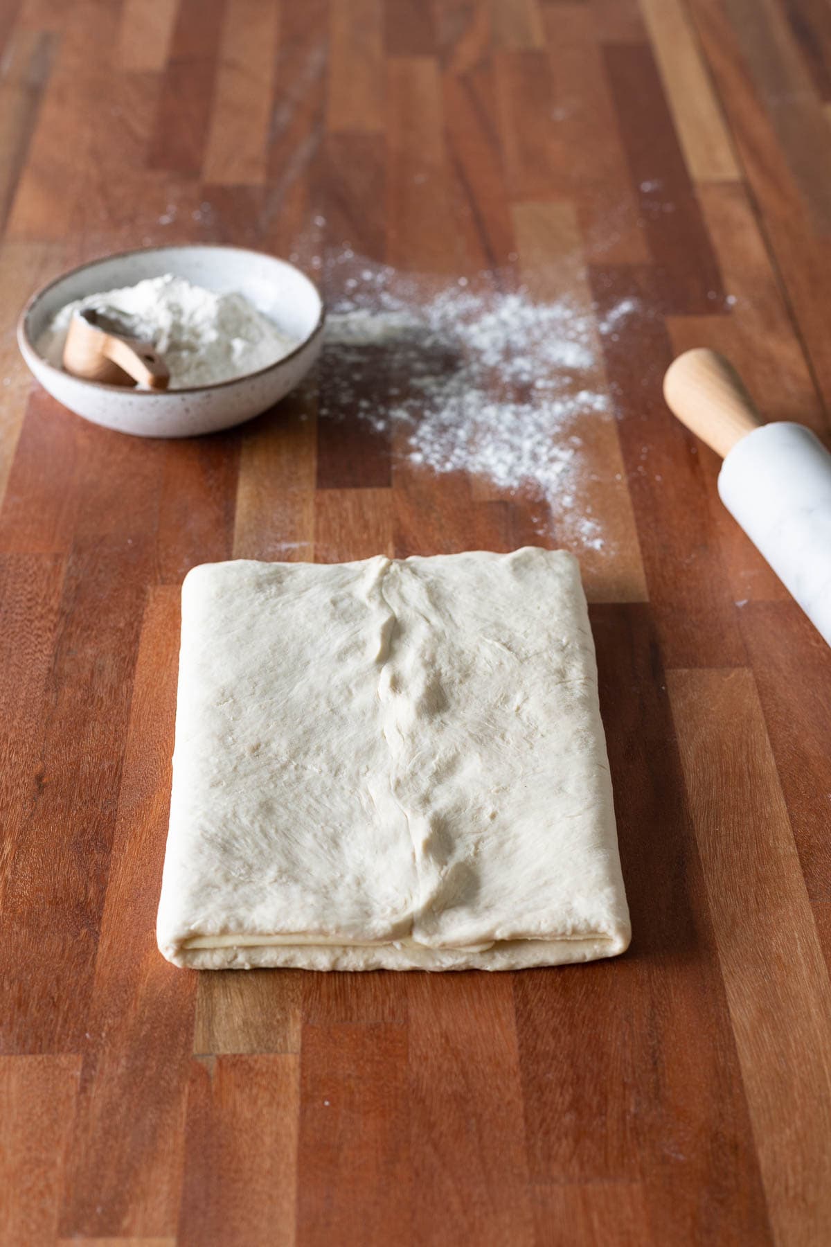 Croissant dough folded like a book with a bowl of flour