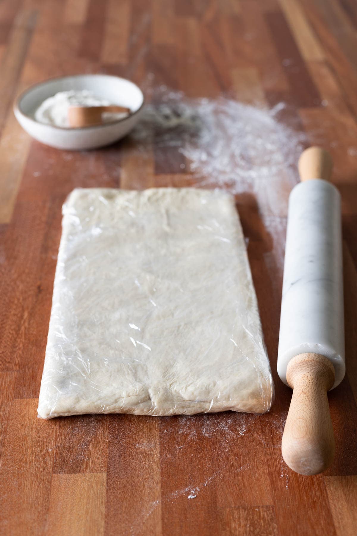 Croissant dough wrapped in plastic wrap with a rolling pin