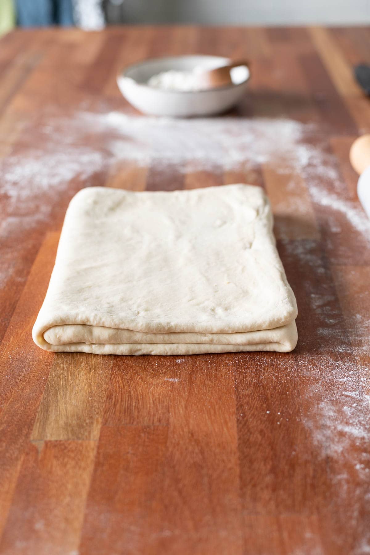 Croissant dough folded like a book with a bowl of flour