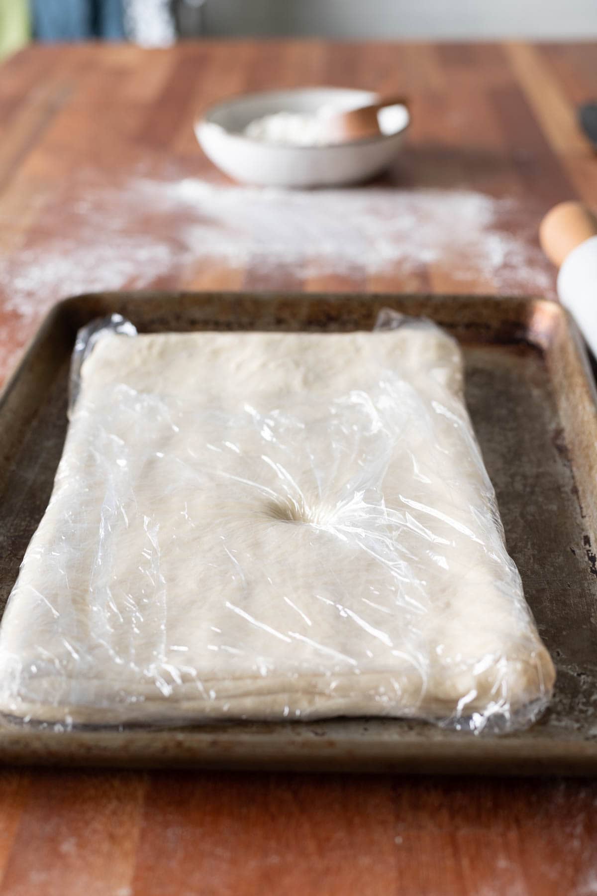 Dough wrapped in plastic wrap on a sheet pan