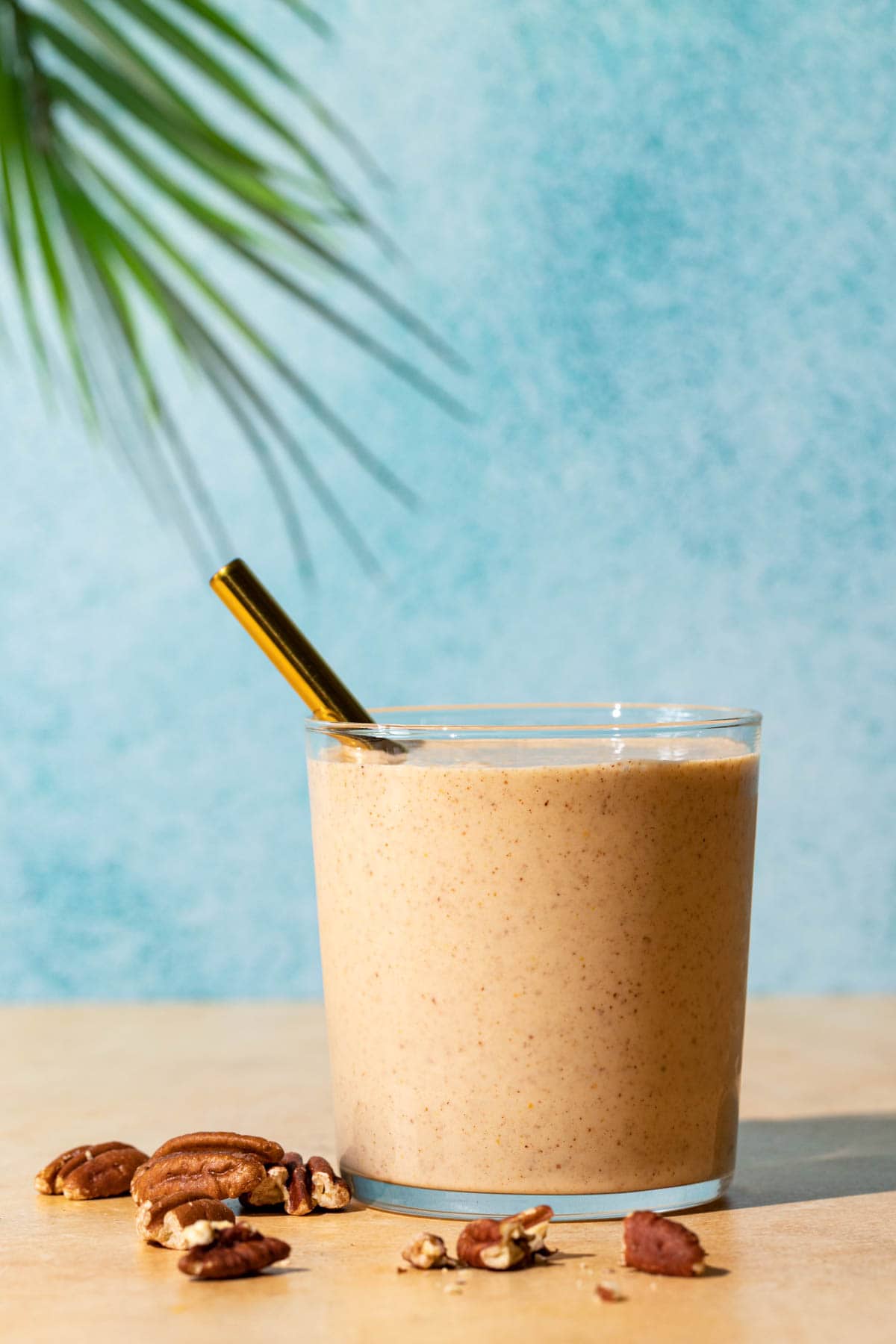 Banana Bread smoothie with crushed toasted pecans in front on a blue and yellow background