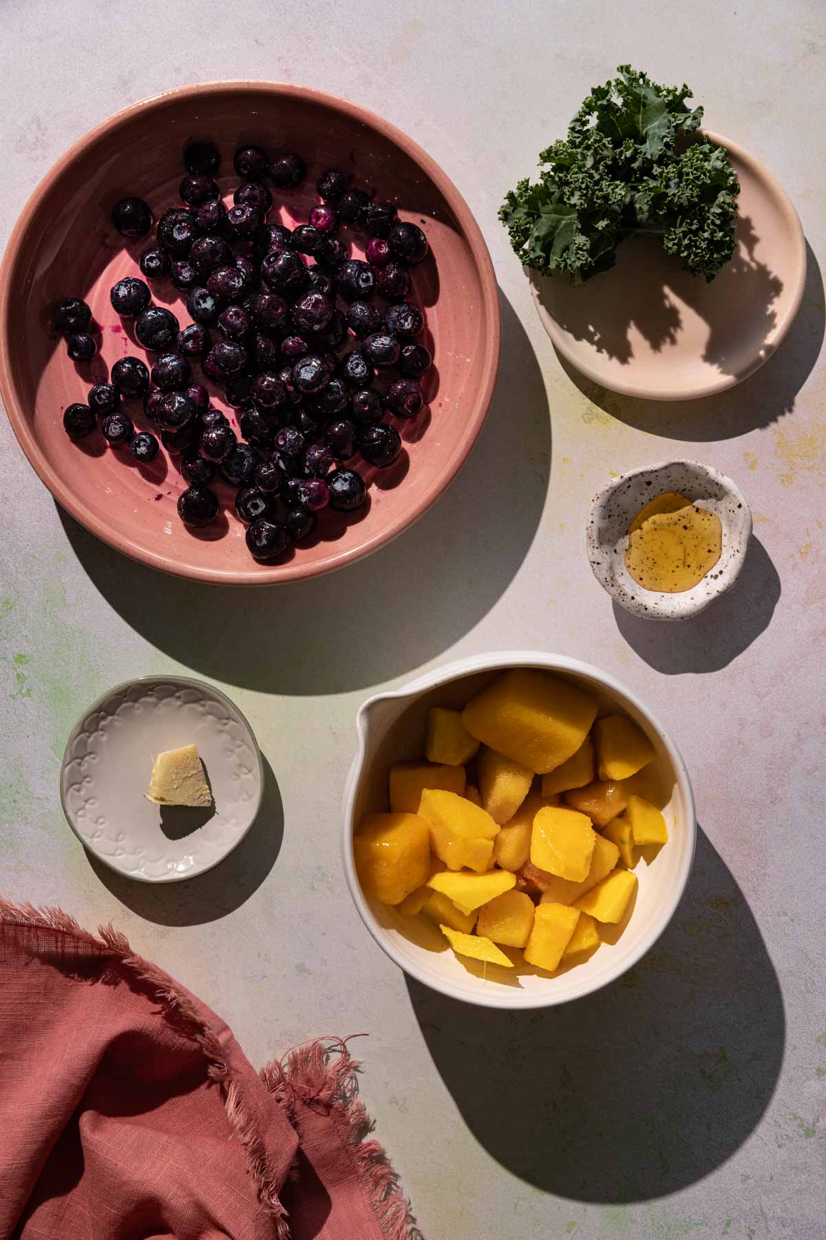 Ingredients for Blueberry Kale smoothie in bowls on a colorful background with a red linen cloth