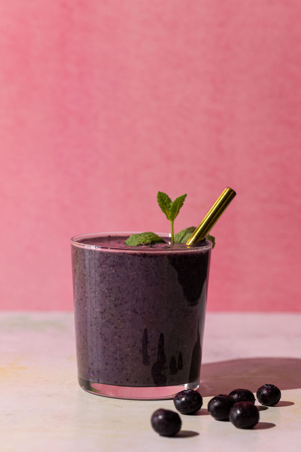 Blueberry Kale smoothie on a pink and white background with blueberries beside glass