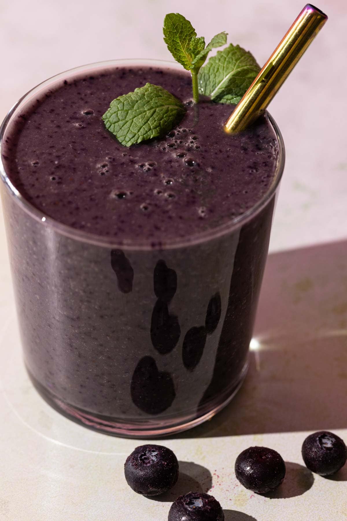Close up of Blueberry Kale smoothie with mint sprig and metallic straw in glass on a colorful background