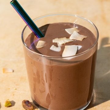 Chocolate coconut smoothie with toasted coconut chips and pistachios on a yellow background