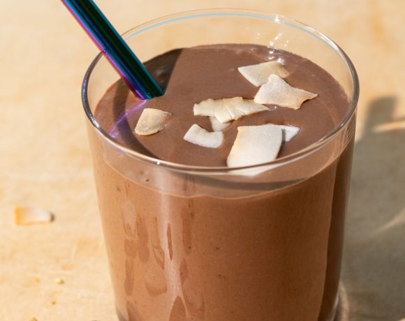 Close up of chocolate coconut smoothie with toasted coconut chips on a yellow background