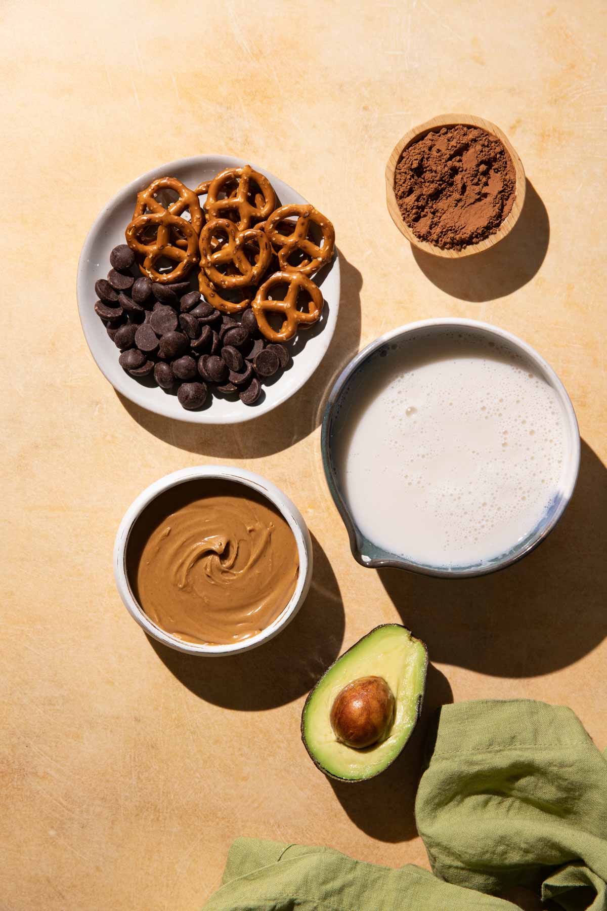 Ingredients for Chocolate Peanut Butter Smoothie in bowls on a yellow background with a green linen cloth