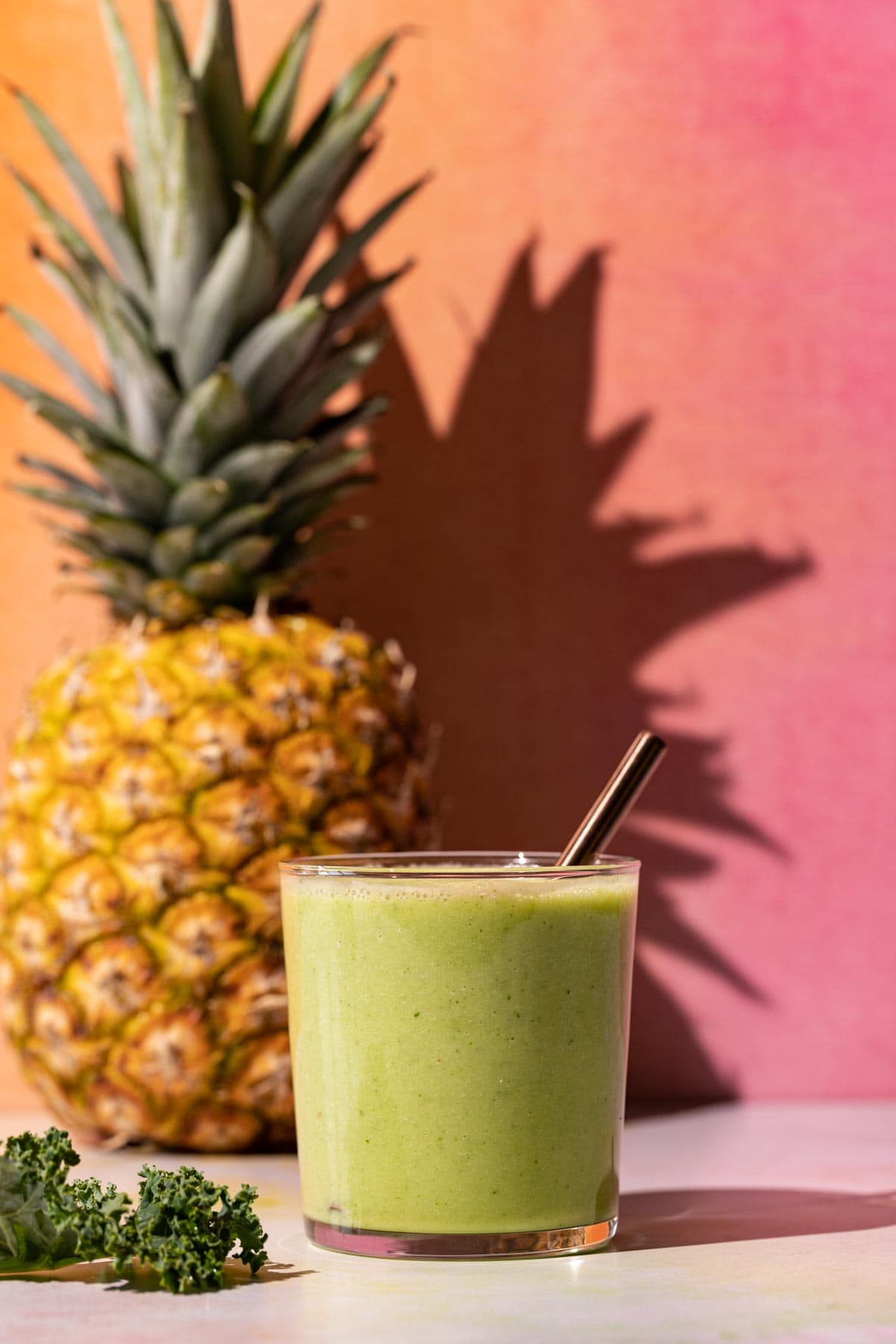 Pineapple Peach smoothie on a colorful background with whole pineapple and kale