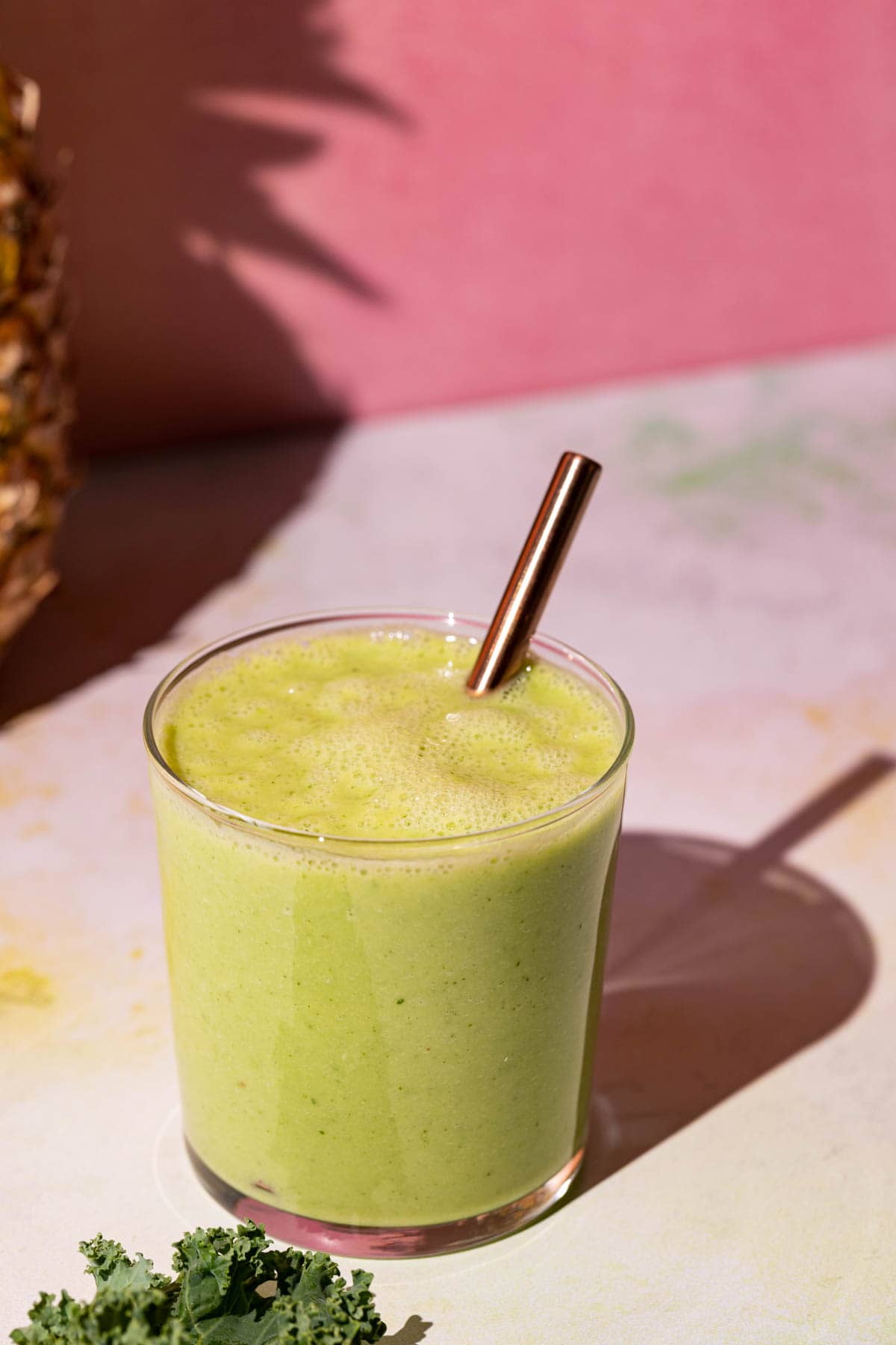 Pineapple Peach smoothie with metallic straw on a colorful background beside kale