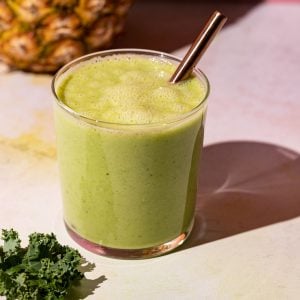 Close up of Pineapple Peach smoothie with kale beside glass on a colorful background