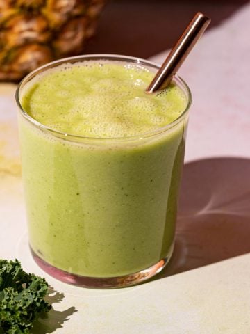 Close up of Pineapple Peach smoothie with kale beside glass on a colorful background