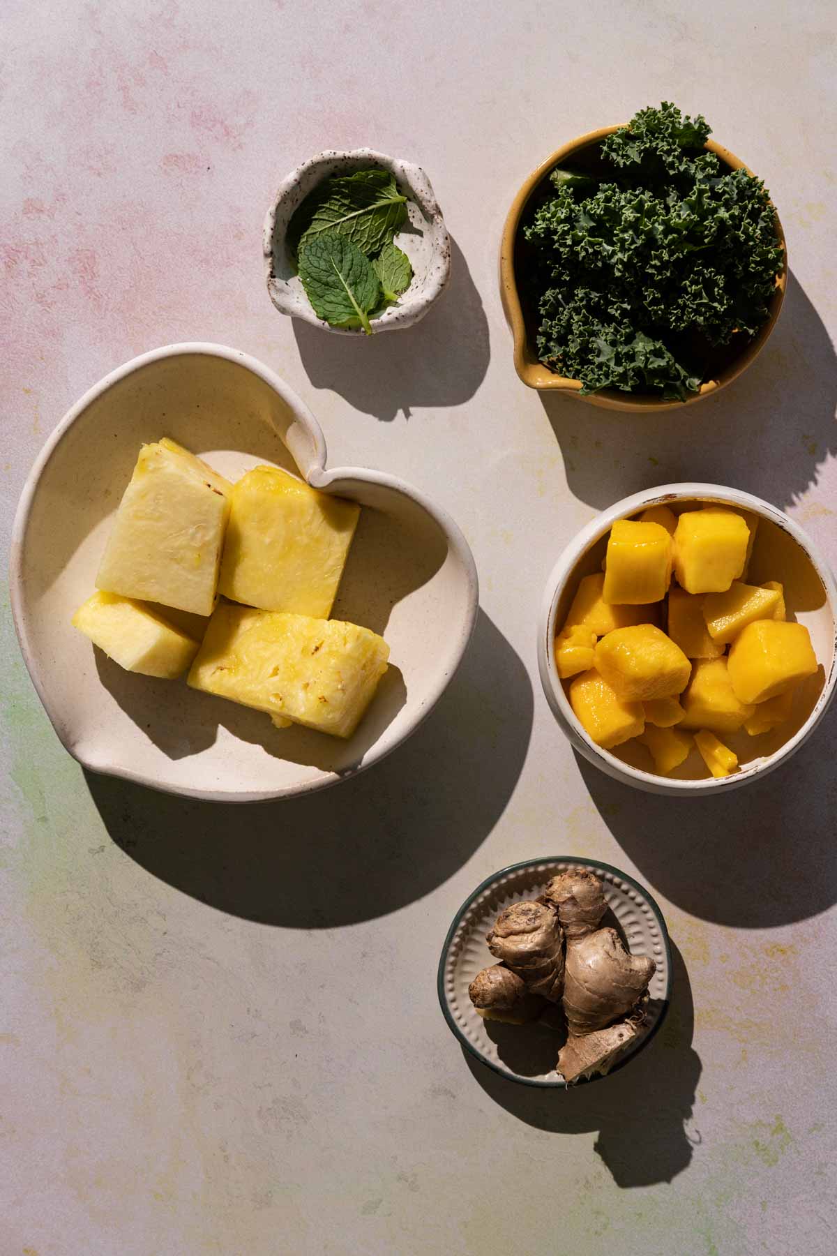 Ingredients for Mango Pineapple Kale smoothie in bowls on a colorful background