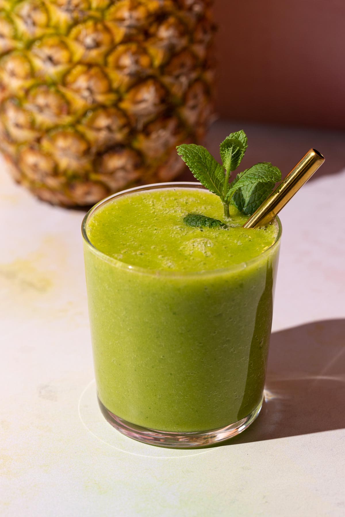 Mango Pineapple Kale Smoothie with a mint sprig in the glass on a colorful background with a pineapple
