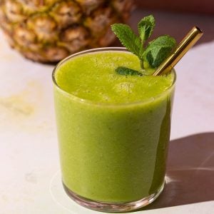 Mango Pineapple Kale smoothie with a gold straw on a colorful background with a pineapple