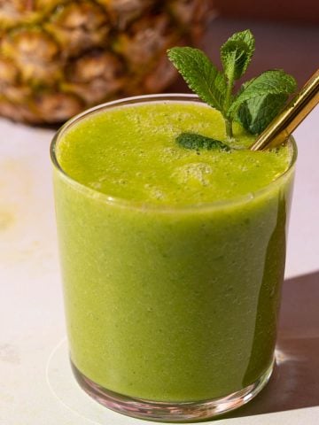 Mango Pineapple Kale smoothie with a gold straw on a colorful background with a pineapple