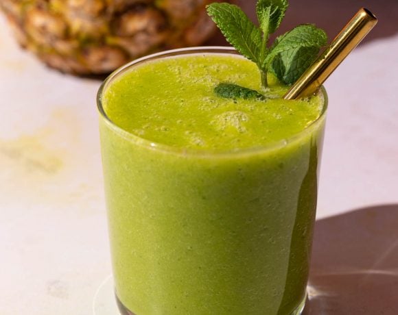 Mango Pineapple Kale smoothie with a gold straw on a colorful background with a pineapple