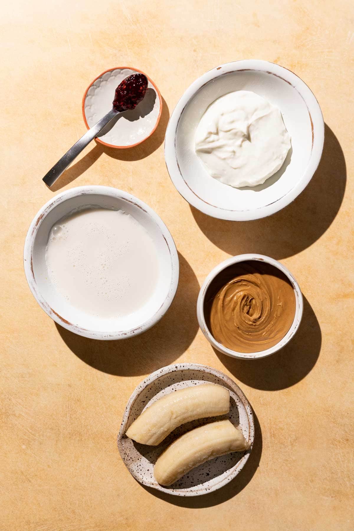 Ingredients for PB&J Smoothie in bowls on a yellow background