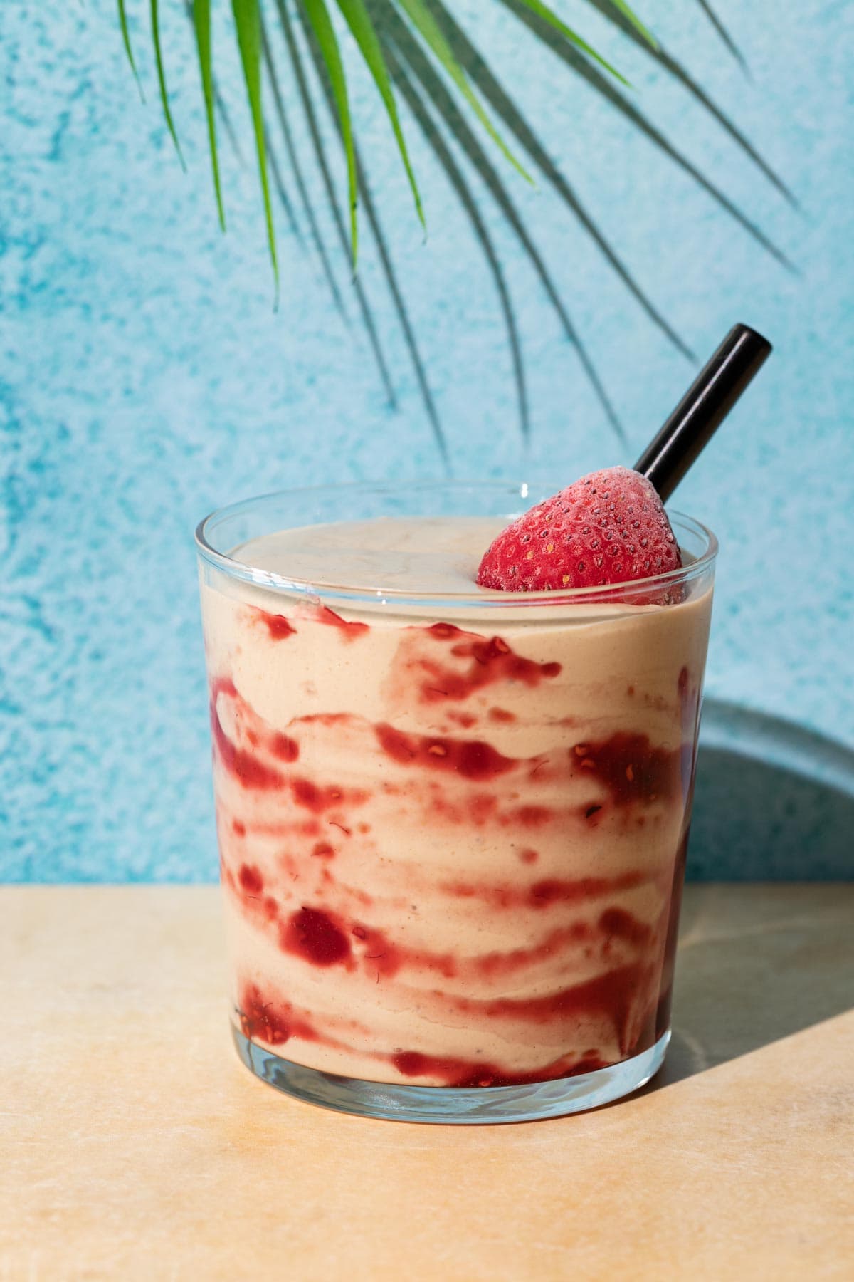 Close up of PB&J Smoothie on a yellow and blue background with a palm leaf overhead