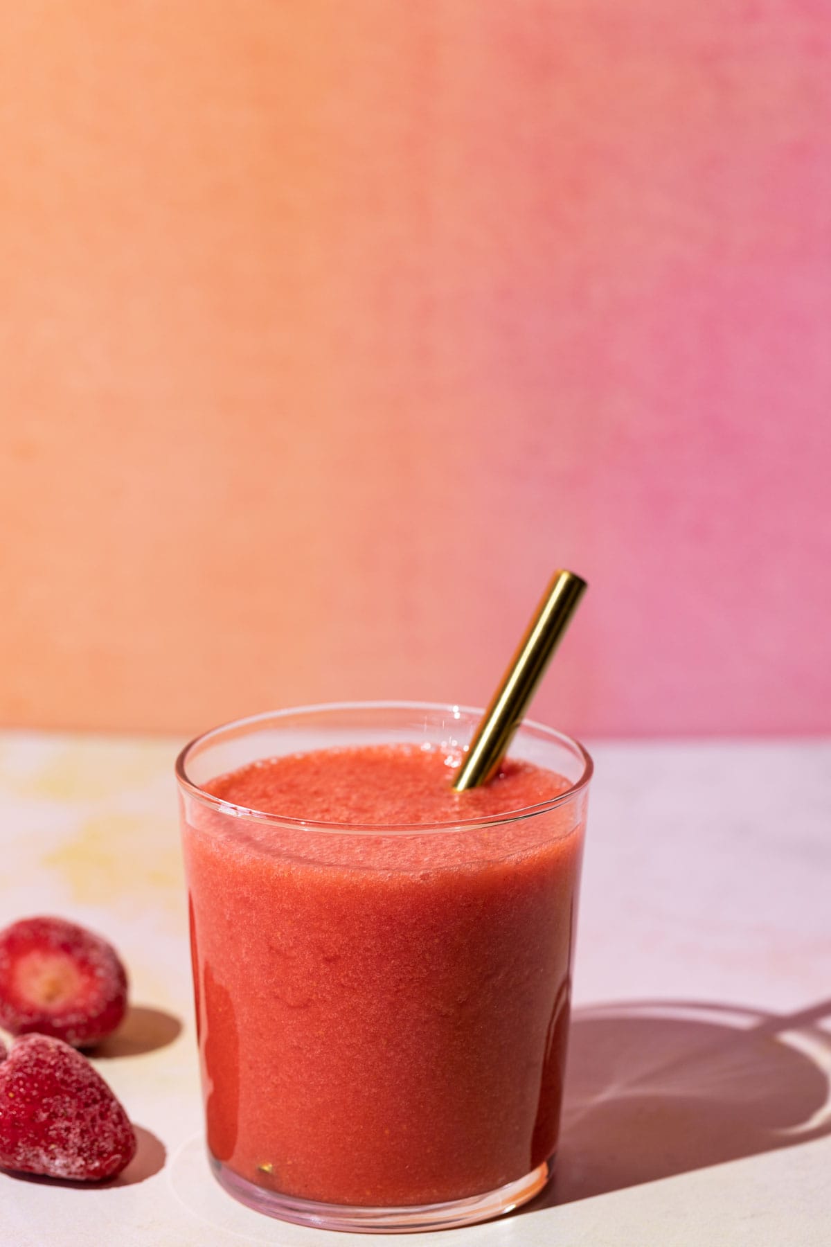 Strawberry lemonade smoothie with strawberries and a gold straw on a colorful background