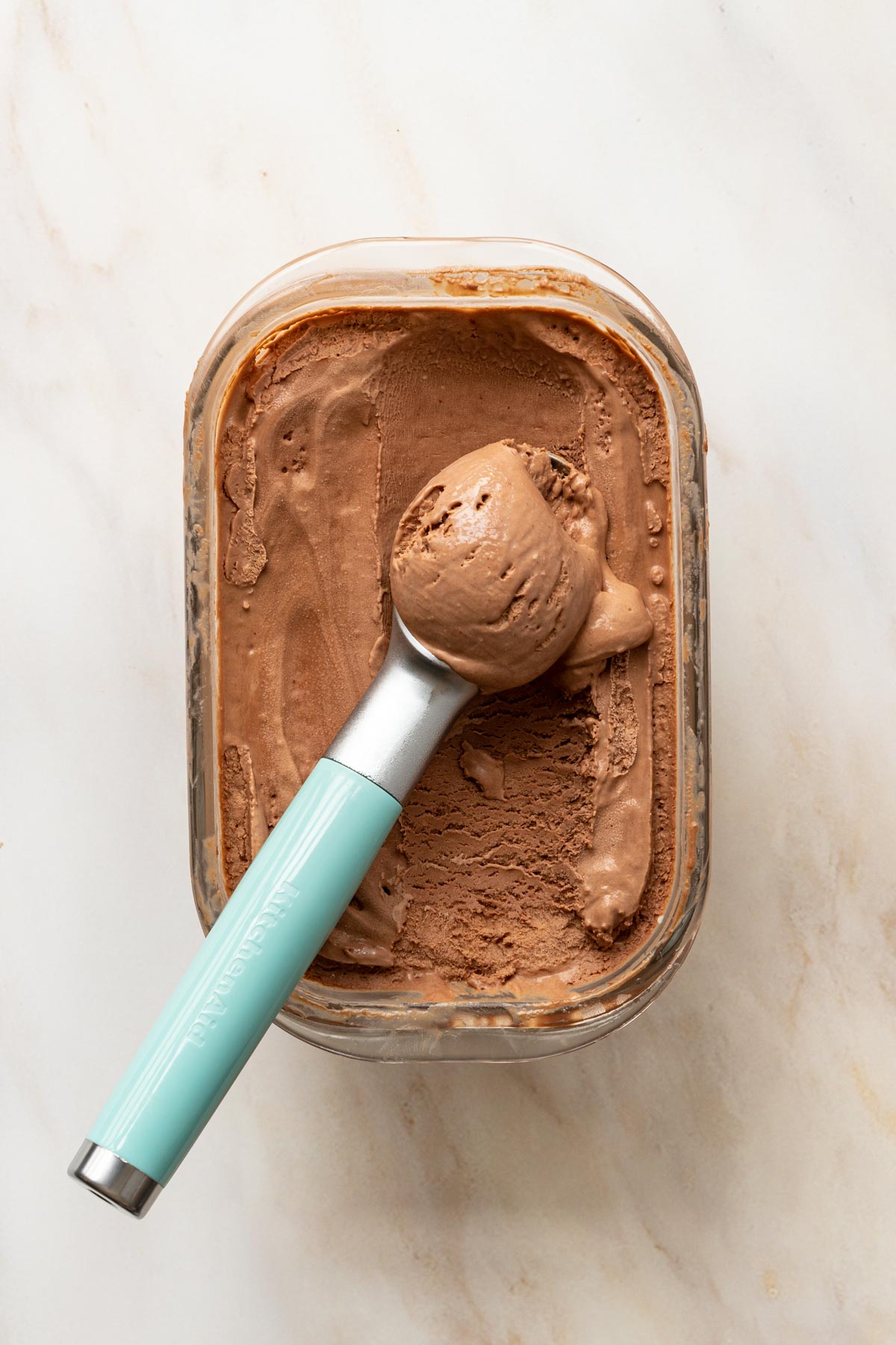 chocolate no churn ice cream in a container with a blue ice cream scoop