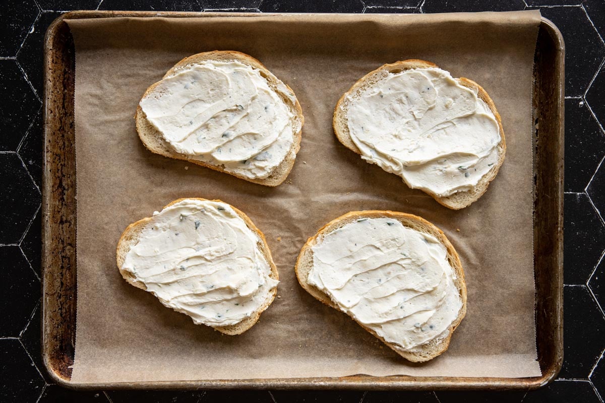 Goat cheese spread on slices of toast on a sheet pan