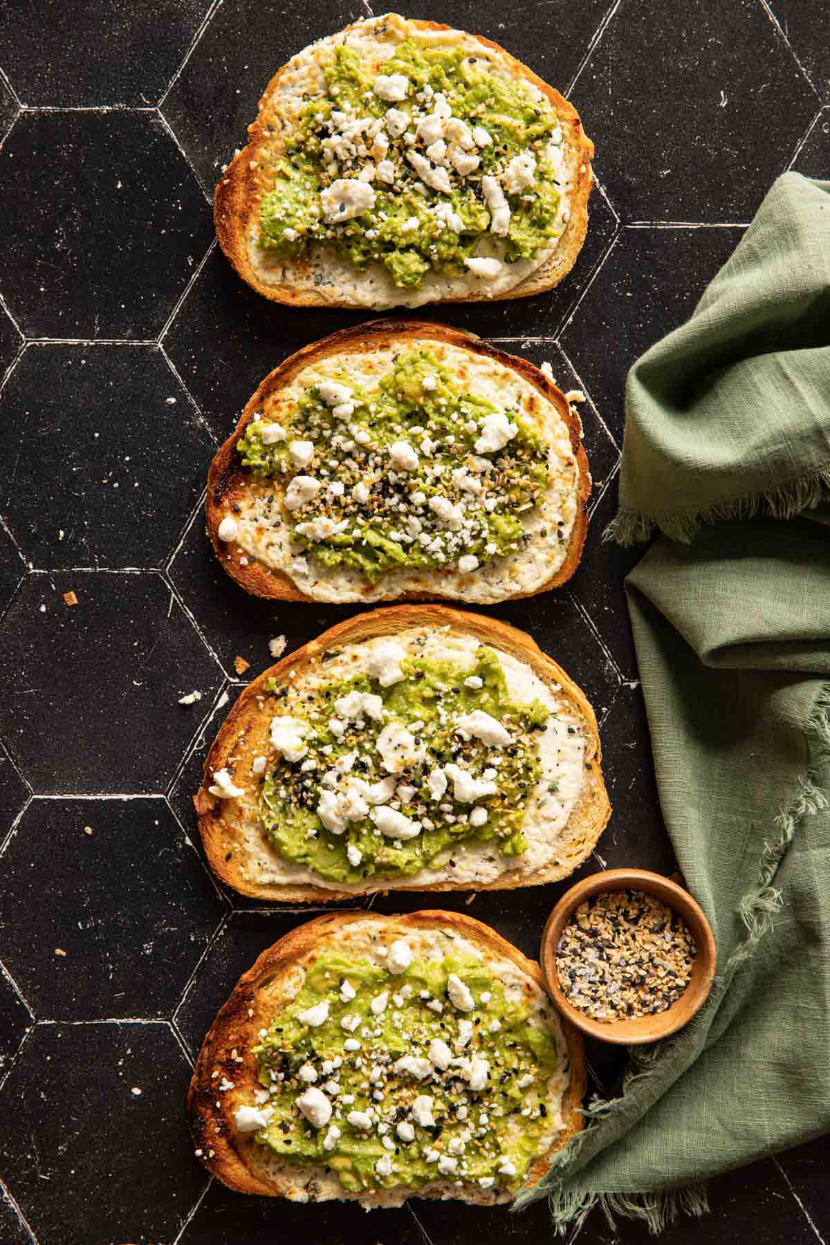 Four goat cheese avocado toasts lined up with a green linen napkin