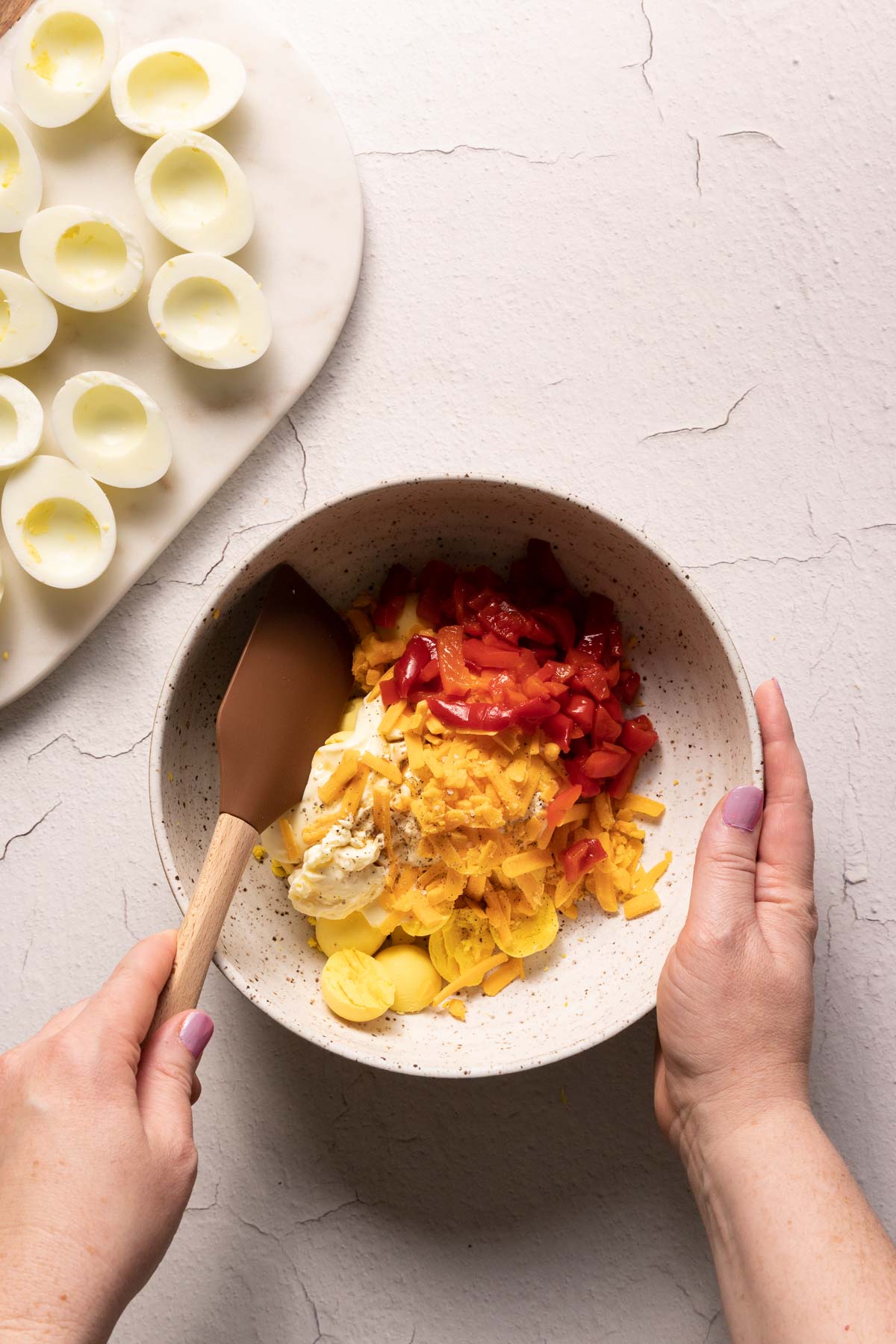 Hands stirring deviled egg ingredients in a bowl