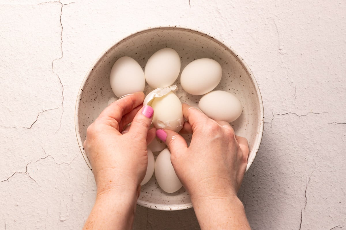 Hands peeling boiled eggs in a bowl