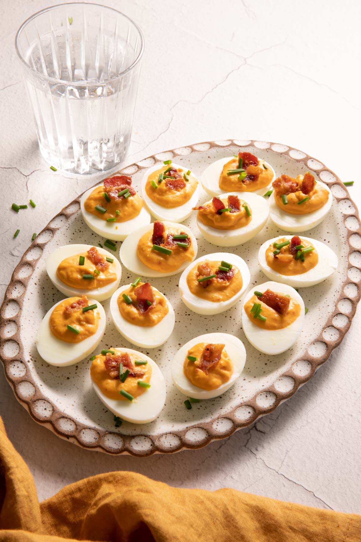 Deviled eggs with bacon on an oval plate and a glass of water