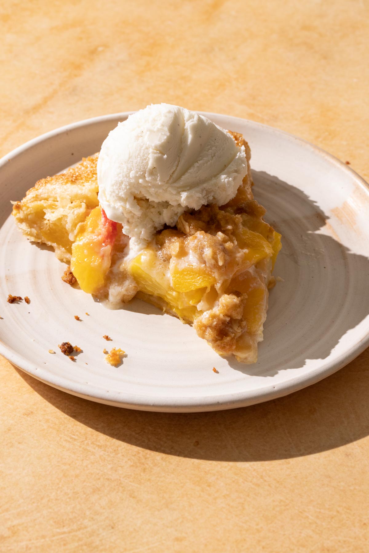 A slice of peach crostata and a scoop of ice cream on a plate