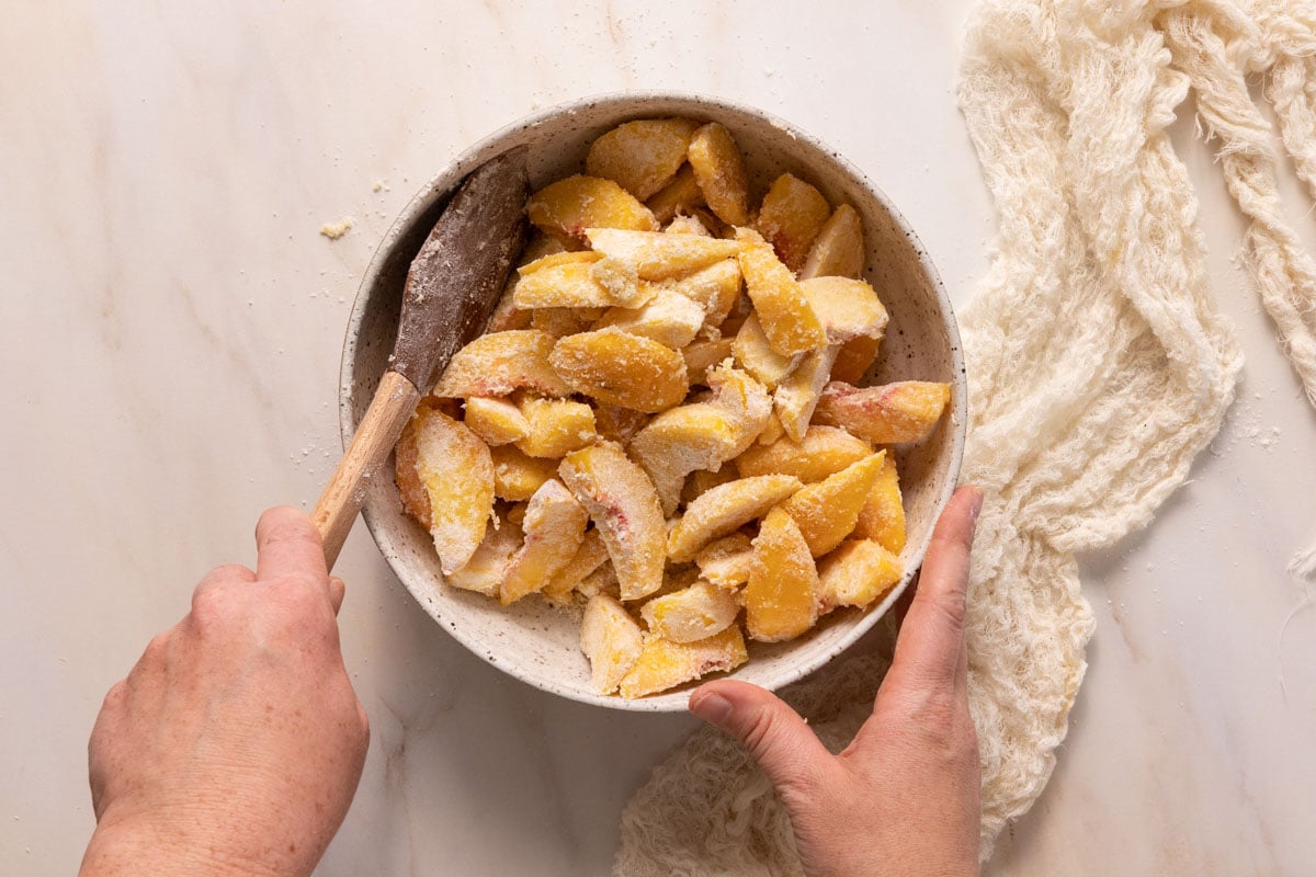 Peaches in a bowl being mixed with flour and sugar