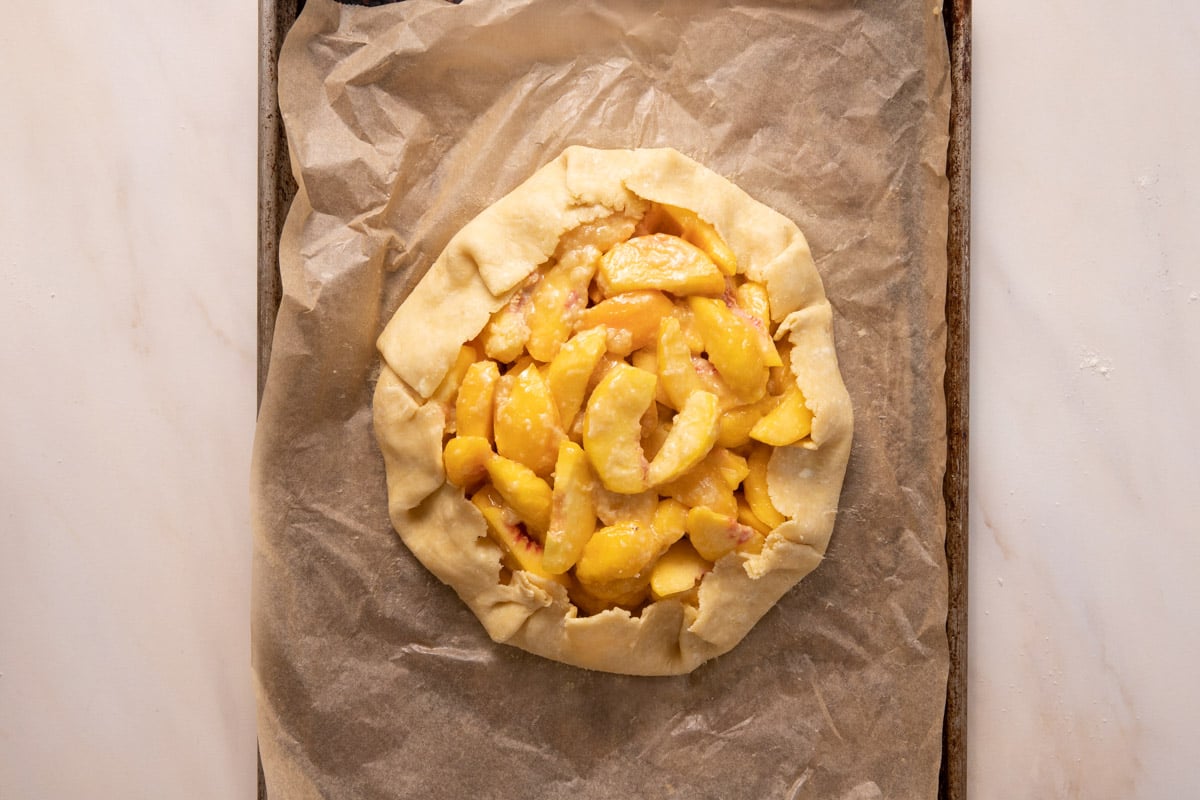 An unbaked Peach crostata on a sheet pan