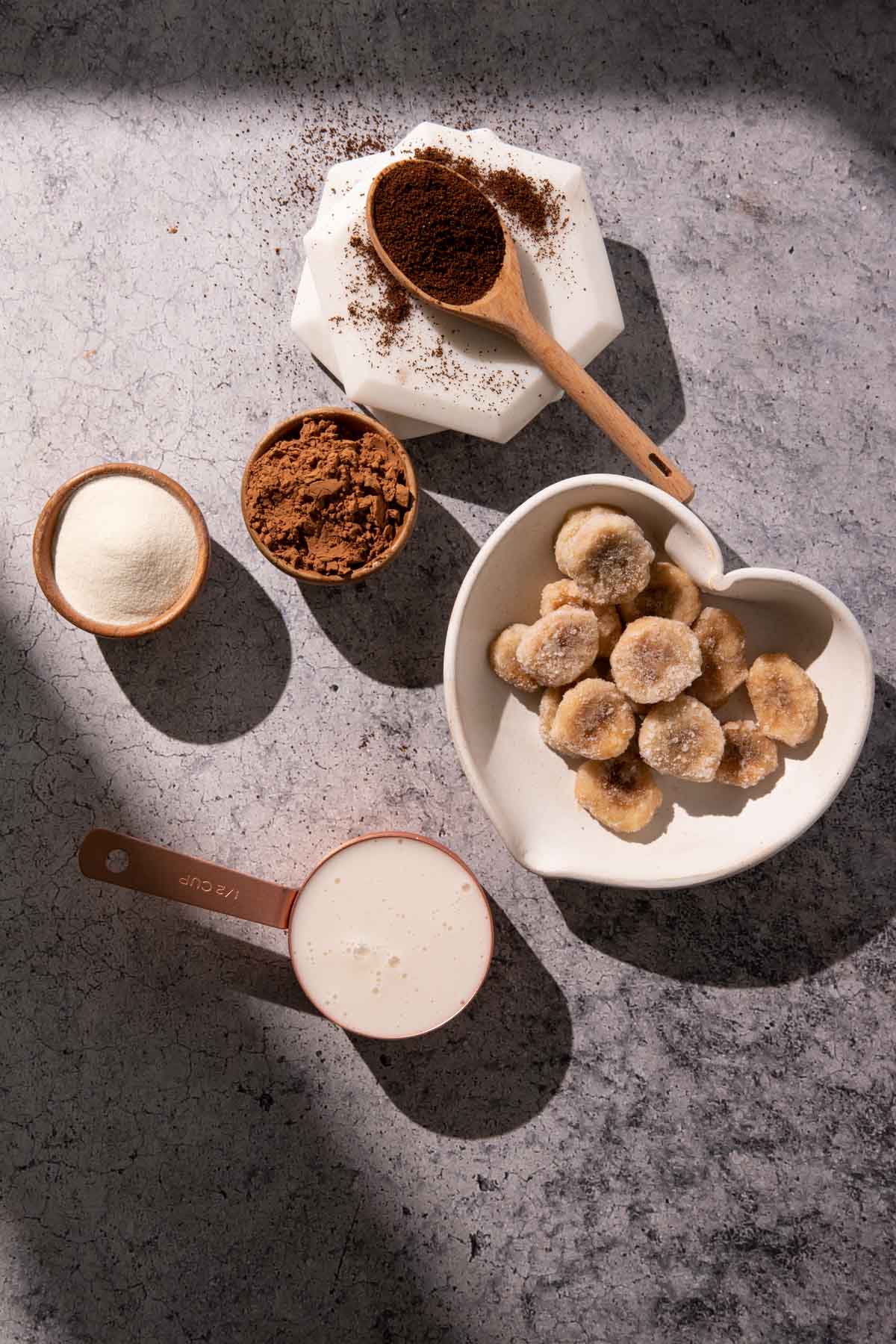 A bowl of frozen bananas, milk, collagen powder, and cocoa powder