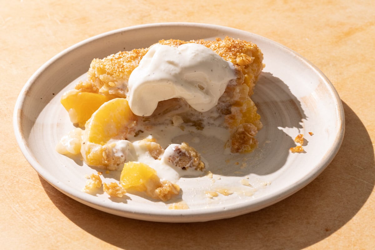 A slice of peach crostata with melted ice cream on a plate